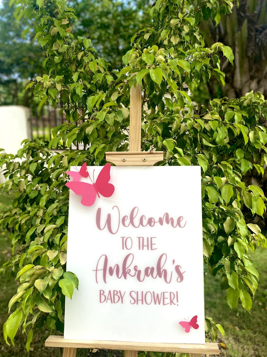 The Petite acrylic welcome sign on a wooden easel, decorated with pink butterflies